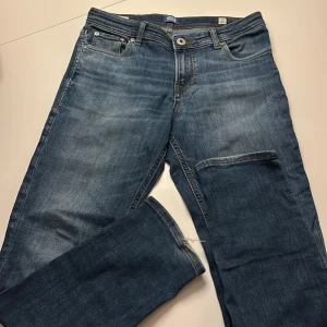 Slim Glenn jeans från Jack & Jones - Snygga blå jeans från Jack & Jones, modell Slim Glenn. Klassisk femficksdesign med smal passform och normal midja. Jeansen har slitningar och kontrastsömmar, tillverkade i mjukt denimtyg som ger en cool look.