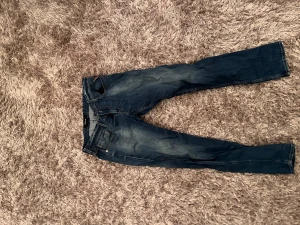 Replay blå jeans - Snygga blå jeans från Replay med klassisk femficksdesign. Jeansen har diskreta slitningar och kontrastsömmar, samt Replay-logga på bakfickan. Materialet är robust denim i bomull. Storlek: W34 L32