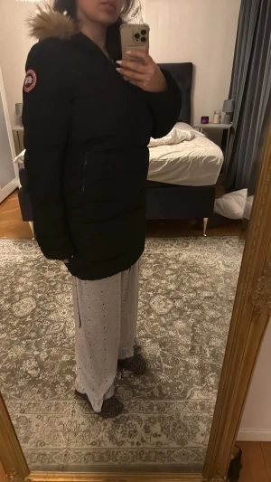 Svart dunjacka från Canada Goose - Säljer min svarta dunjacka från Canada Goose med fluffig päls på huvan och klassisk logga på ärmen. Jackan är lång, har dragkedja framtill och är perfekt för kalla vinterdagar. Snygg, stilren och riktigt varm med en loose passform.