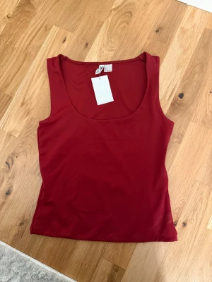 Röd ärmlös linnetopp från H&M - Snygg röd linnetopp från H&M med rundad halsringning och ärmlös design. Perfekt för att skapa en enkel och stilren look. Tillverkad i mjuk polyester som känns skön mot huden.