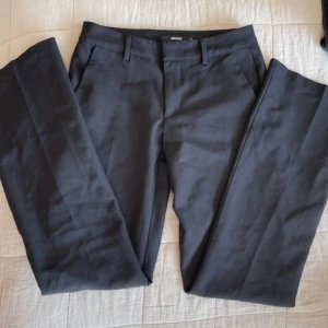 Lågmidjade kostymbyxor från BikBok - Klassiska svarta kostymbyxor från BikBok i storlek 34. Byxorna har raka ben, hällor för bälte och diskreta fickor både fram och bak. Perfekta för en clean look. Materialet känns mjukt och har en lätt stretch för extra komfort. 🌸