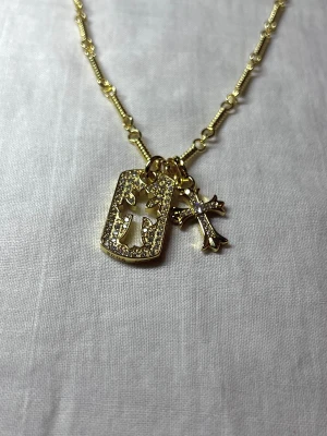 Rockstar Aureate Cross - Golden necklace with a sparkling tag (2.4 × 1.4 cm) and cross charm (1.9 × 1.4 cm). 55 cm chain, fully adjustable along its length.