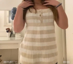 Randig beige och vit blus med knappar Hollister  - Supersöt blus med breda beige och vita ränder, urringad  halsringning och små knappar framtill. Modellen är lite längre och har korta ärmar. Materialet är ribbat och känns mjukt mot huden. Från Hollister vintage 