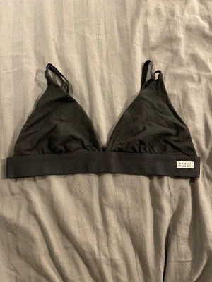 Svart linnetopp från Frank Dandy - Svart linnetopp från Frank Dandy med smala axelband och bred resår under bysten. Toppen har triangelformade kupor och justerbar knäppning bak. Perfekt för en chill och enkel stil.