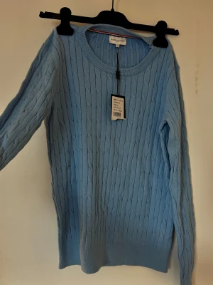 Ljusblå stickad tröja från Panos Emporio - Snygg ljusblå stickad tröja från Panos Emporio med kabelstickat mönster. Rund halsringning och långa ärmar ger en klassisk look. Perfekt att matcha med jeans eller kjol för en chill och stilren vibe. Storlek 158/164 men passar lätt S/Xs. Org pris; 799kr 