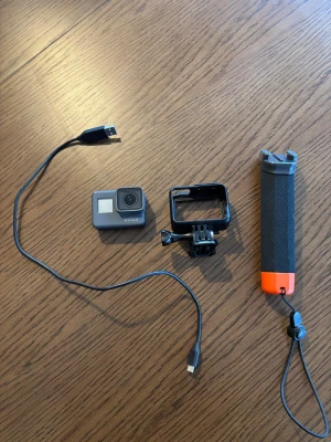 GoPro HERO actionkamera med tillbehör  - GoPro HERO actionkamera i fint skick, komplett med skyddande ram, flytande handtag och laddkabel. Perfekt för äventyr och vattensport. Inga synliga repor eller skador, allt fungerar som det ska. Enkel att använda och robust design.