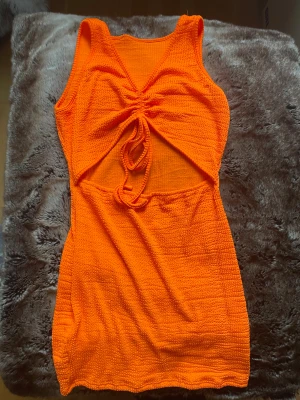 Orange kortklänning med snörning - Säljer en cool orange kortklänning med snörning och cut-out detaljer framtill. Klänningen är ärmlös och har en texturerad, stickad känsla i materialet. Perfekt för dig som gillar färgstarka och unika plagg med snygga detaljer.