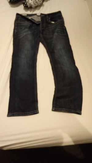 Mörkblå jack & Jones jeans straight fit - Säljer ett par mörkblå jeans från Jacke & Jonas  med klassisk straight fit. Jeansen har snygga slitningar, fem fickor och detaljerade sömmar. Materialet är robust denim och passformen är normal. Perfekt för dig som gillar en tidlös jeansstil.