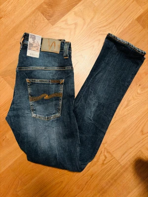 Nudie Jeans Tape Ted  - Säljer ett par Nudie Jeans Tape Ted i tvättad blå denim. Jeansen är helt oanvände med prislapp kvar. Perfekt för dig som vill ha personsanpassade jeans. L34 men passar även kortare då de är slim och hyperflex material. Skriv gärna vid minsta fundering! 