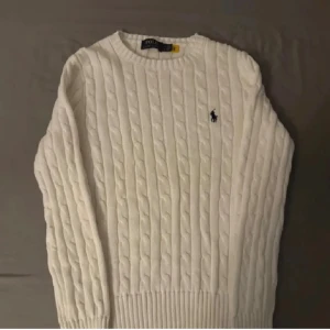 Kabel stickad från Ralph lauren  - Snygg vit kabelstickad tröja från Polo Ralph Lauren i mycket bra skick. Klassisk modell med svart broderad logga. Mjuk, skön och perfekt för både vardag och finare tillfällen. Inga skador eller fläckar