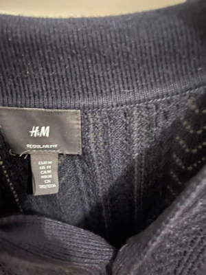 Mörkblå stickad pikétröja H&M M - Snygg mörkblå stickad pikétröja från H&M i regular fit. Tröjan har klassisk krage och korta ärmar, med ett diskret mönster i stickningen som ger extra stil. Perfekt för dig som gillar en chill och clean look.