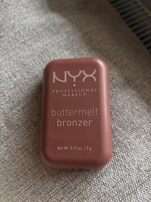 NYX Buttermelt Bronzer Butta Off - NYX Buttermelt Bronzer i nyansen Butta Off (BMB05), en medium-djup varm rosig ton. Kommer i en kompakt, brun plastförpackning. Krämig formula som smälter in i huden och ger en naturlig solkysst look. Innehåller bland annat sheasmör och solrosolja.