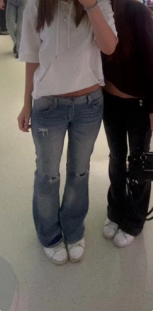 Blå bootcut jeans med slitningar - Säljer ett par blå bootcut jeans med snygga slitningar vid knäna och låren. De har låg midja och klassisk femficksdesign. Jeansen är i denim och har en cool, avslappnad vibe som passar perfekt till sneakers.