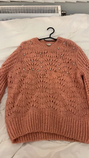 Rosa stickad tröja River Island - Superfin stickad tröja från River Island i en varm rosa ton. Tröjan har ett snyggt mönster och är dekorerad med pärlor och små glittriga detaljer framtill. Den har långärmad passform. Passar storlek S/M