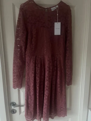 Rosa spetsklänning från Vila - Supersöt rosa spetsklänning från Vila med långärmad design och blommigt spetsmönster. Klänningen har rund halsringning och är i kort modell. Perfekt för dig som vill ha en romantisk och feminin look.