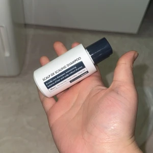 Scalp DX Scaling Shampoo 50ml - Scalp DX Scaling Shampoo från Dr. Ceuracle i en smidig 50ml flaska med mörkblått lock. Perfekt för att balansera hårbotten och ge glansigt hår utan torrhet. Flaskan är vit med tydlig etikett och text på både engelska och koreanska.