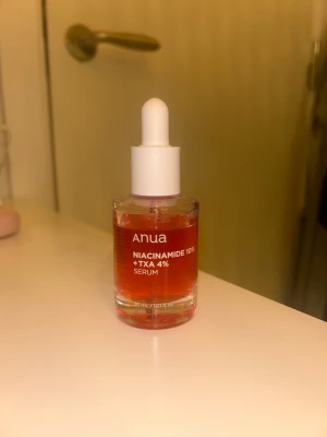 Anua Niacinamide 10% + TXA 4% Serum - Säljer ett Anua Niacinamide 10% + TXA 4% serum i en genomskinlig glasflaska med vit pipett. Serumet har en snygg orange-röd färg och kommer i 30 ml storlek. Perfekt för dig som vill boosta din hudvårdsrutin med niacinamid och tranexamsyra. Använd 1 gång.💕 Nypris 340kr.
