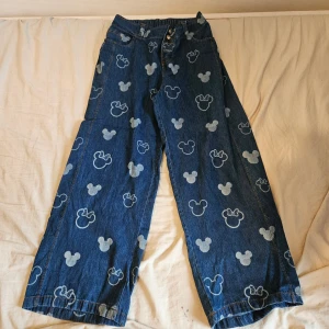 Blå jeans med Mickey Mouse-mönster - Mörkblåa mickey mouse byxor som har stretchig midja och.är helt oanvända! Storlek 152, blir större pga stretch.