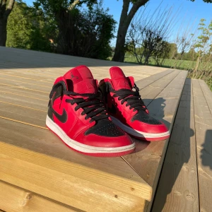 Air Jordan 1 mid i rött och svart - Snygga Nike Air Jordans i en klassisk röd och svart färgkombination. Skorna har en rund tå och snörning framtill. Perfekta för dig som vill ha en stilren och sportig look. Nypris är 2200kr