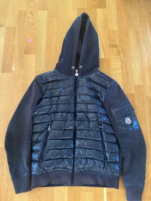 Mörkblå Moncler pufferjacka med huva - Säljer en mörkblå pufferjacka från Moncler i storlek S. Jackan har quiltad framsida i glansigt material, mjuka ärmar och huva med snörning. Ficka med Moncler-logga på ärmen och dragkedjor på fickorna framtill. Perfekt för kyliga dagar. Skriv om ni har frågor eller funderingar!😊