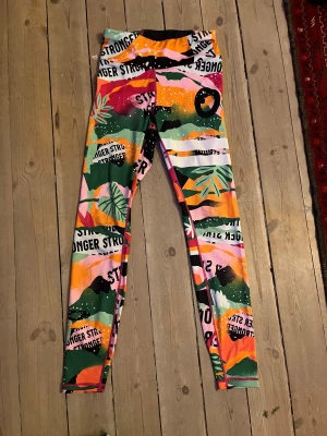 Färgglada leggings från Stronger - Säljer ett par leggings från Stronger med ett riktigt färgstarkt och coolt mönster i orange, rosa, grön, svart och vitt. Har en ficka bak också.