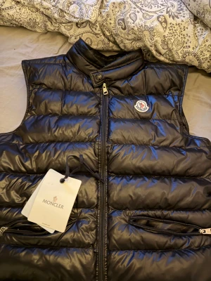 Äkta Moncler Gui Väst  - Storlek 2, säljes pga att den är för liten. Inga slitage alls, stort sett nyskick. Tags och svart moncler påse följer med