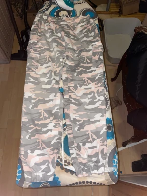 Cargopants i rosa och grå camo - Säljer ett par mjuka cargopants från Asu i storlek 36 med rosa, grå och vit camouflage-mönster. Byxorna har elastisk midja med snörning och praktiska fickor på sidorna. Perfekt för en chill och avslappnad stil.