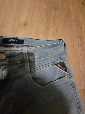 Replay ljusblå jeans straight fit - Snygga ljusblå jeans från Replay med klassisk femficksdesign och raka ben. Jeansen har en stilren look med diskreta sömmar och Replay-logga på fickan. Perfekt för dig som gillar en enkel och clean stil. Materialet är mjukt jeans och midjan är normal.