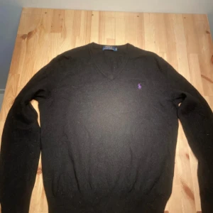 Svart kashmirtröja Polo Ralph Lauren - Svart v-ringad tröja från Polo Ralph Lauren i mjuk merinoull. Tyvärr 1 hål i vänstra armhåla. Går att laga billigt hos skräddare. Storlek M, skulle säga att den passar S bättre.