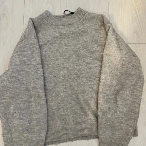Grå stickad tröja från H&M XS - Mysig grå stickad tröja från H&M i storlek XS. Tröjan har en klassisk rund halsringning och ribbade muddar vid ärmslut och nederkant. Perfekt för lager-på-lager och chill dagar.