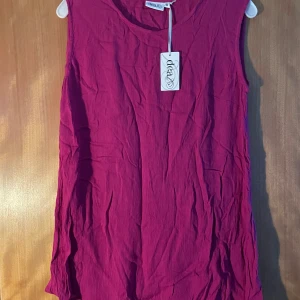 Cerise ärmlös linnetopp från Idea - Säljer en cerise ärmlös linnetopp från Idea med rund halsringning. Toppen har en lätt skrynklig struktur och är tillverkad i ett mjukt material som känns luftigt. Perfekt för varma dagar och enkel att matcha med jeans eller shorts.