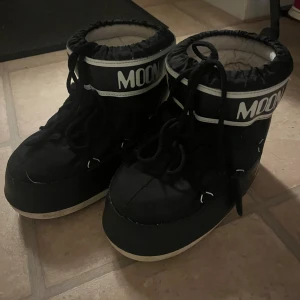 Svarta Moon Boots - Moon Boots i svart med vit logga och även med vadderad insida för extra värme. Perfekta för vintern och har en ikonisk chunky siluett som sticker ut. Använda fåtal gånger förra vintern. Dom passar alla storlekar från 37-40 skulle jag säga! 