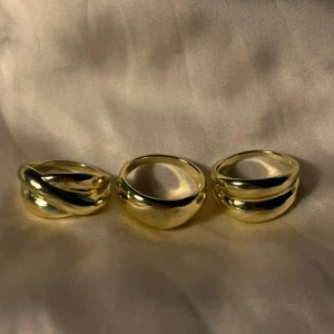 3 chunky guldiga ringar - Säljer ett set med tre chunky ringar i guldigt metall. En ring har tvinnad design, de andra två har slät och bred form med en lätt böjd kant. Perfekt för dig som gillar statement-smycken och vill addera lite extra bling till din stil.