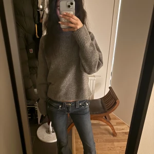 True Religion lågmidjade bootcut jeans - Säljer ett par mörkblå jeans från True Religion med låg midja och bootcut-snitt. Jeansen har klassiska kontrastsömmar, stora fickor med lock och knappdetaljer bak samt logopatch i vitt. Materialet är slitstarkt denim och passformen är loose.