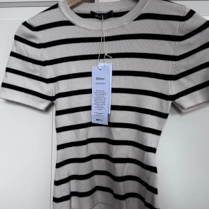 Randig stickad topp från Gina Tricot - Säljer en snygg stickad topp från Gina Tricot i storlek S. Toppen är vit med svarta horisontella ränder, har rund hals och korta ärmar.  Passformen är normal och toppen är riktigt skön mot huden. Aldrig använd. Ordpris 259kr. SKRIV INNAN KÖP!