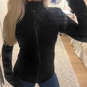 Lululemon define jacket - Säljer en svart, slim träningsjacka från Lululemon med hög krage och hel dragkedja framtill. Jackan har långa ärmar och två sidofickor med dragkedja. Perfekt för dig som gillar sportig och clean stil. Är i storlek S men passar Xs och M också 