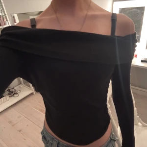 Svart offshoulder topp - Säljer en svart offshoulder topp med lång ärm. Toppen har en bred kant över axlarna som ger en snygg och modern look. Perfekt att styla med jeans eller kjol för en cool och snygg vibe.