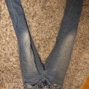 Blå skinny jeans i denim, 32/32 - Säljer ett par blå skinny jeans i klassisk denim med snygga slitningar på framsidan. Modellen har smal passform och raka bakfickor, perfekt för dig som gillar en tajt look. Jeansen har gul kontrastsöm och är tillverkade i bomullsmaterial.