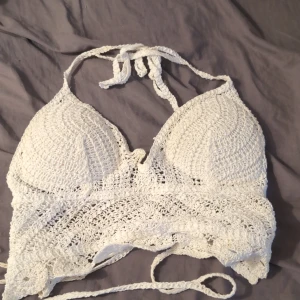 Vit virkad strandtopp med knyt - Superfin vit strandtopp i virkad stil med knyt i nacken och runt ryggen. Snygg boho-vibe och perfekt för stranden eller poolen. Mjuk och luftig känsla, passar dig som vill sticka ut lite extra i sommar.