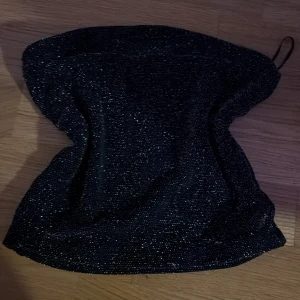 Glittrig svart tubtopp  - Säljer en snygg svart tubtopp från Sister i storlek XXS. Toppen har glittriga detaljer som ger en extra cool vibe och är axelbandslös med bandeau-form. Perfekt för dig som vill sticka ut med en enkel men glammig look. Säljer på grund av att den blivit för liten för mig. Kontakta för flera frågor och funderingar 🥰