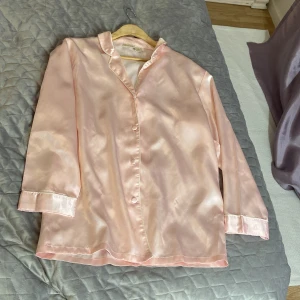 Ljusrosa satinblus från Exclussiv - Ljusrosa blus i glansigt satinmaterial från Exclussiv. Klassisk krage, knäppning framtill och långa ärmar. Snygg och stilren med en mjuk känsla och lätt oversized passform. Perfekt för dig som gillar en chic och enkel look.passar 38-40