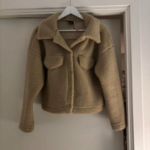 Beige teddyjacka från Gina Tricot - Supermysig teddyjacka i beige från Gina Tricot, med krage och två bröstfickor. Jackan har en loose passform och är tillverkad i mjuk fleece. Är i storlek S men passar även XS. Perfekt för dig som gillar chill och comfy stil. Långärmad och stängs med knappar framtill. Den översta knappen har lossnat men den är lätt att sy på, man tänker inte på att den är loss. Priset går att diskutera, skriv bara om du har frågor💗💗