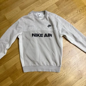 Grå Nike Air sweatshirt i bomull - Snygg grå Nike Air sweatshirt med svart logga både fram och bak. Tröjan har långärmade vita paneler på sidorna och ribbade muddar. Perfekt för dig som gillar sportig och clean stil. Mjuk insida i bomullsmix för extra komfort.