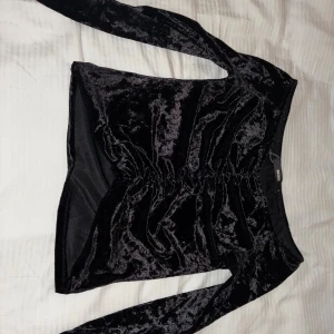 Svart sammetstopp med snörning från Bik Bok - Säljer en svart långärmad topp från Bik Bok i glansig sammet. Toppen har snygg snörning framtill som ger en cool rynkad effekt och är croppad i modellen. Perfekt för dig som gillar statement-plagg med lite edge.