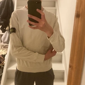 Beige Stone Island sweatshirt - Säljer en beige långärmad sweatshirt från Stone Island Junior med klassisk patch på ärmen. Tröjan har rund halsringning och ribbade muddar. Perfekt för dig som gillar clean streetwear och vill ha något stilrent med ikonisk logga. Storlek 10-12 år, köpt på Nk och säljer pga att jag har växt ur den.