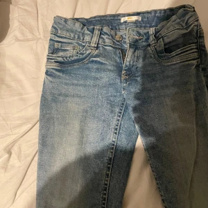 Ljusblå jeans från Gina Tricot - Säljer ett par ljusblå jeans från Gina Tricot i klassisk femficksmodell. Jeansen har normal passform och raka ben, med dragkedja och knapp framtill. Perfekta till vardags och lätta att matcha med olika stilar.