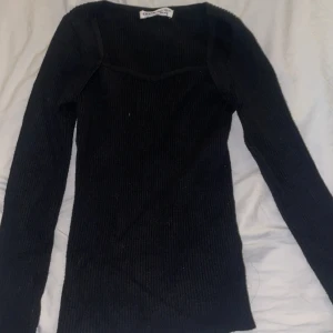 Svart ribbad stickad tröja  - Svart långärmad stickad tröja från Chiquelle med ribbad struktur och snygg v-ringad hals. Modellen är slim och sitter tajt mot kroppen, perfekt för dig som gillar en stilren och enkel look. Passar till jeans eller kjol för en cool vibe.