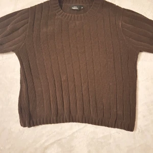 Brun ribbstickad tröja KappAhl XS - Mysig brun ribbstickad tröja från KappAhl i storlek XS. Tröjan har rund halsringning och halvlånga ärmar, perfekt för kyligare dagar. Den är stickad i ett mjukt material och har en klassisk, enkel design som är lätt att matcha.