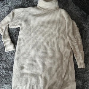 Beige stickad poloklänning Gina Tricot - Mysig beige stickad poloklänning från Gina Tricot i storlek XL. Klänningen har lång ärm, ribbad struktur och hög polokrage. Perfekt för dig som gillar oversized och comfy vibes under kyliga dagar.