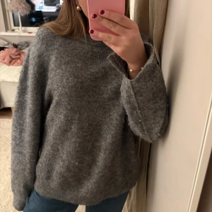 Grå stickad tröja med lång ärm - Grå stickad tröja i bra skick, tröjan har en liten slott bak i ryggen, den är avsiktlig